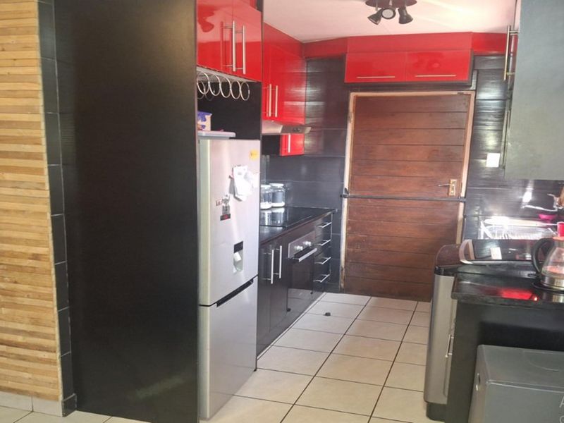 A compact kitchen featuring high-gloss red and black cabinetry, tiled flooring, and a wooden door leading to the exterior.