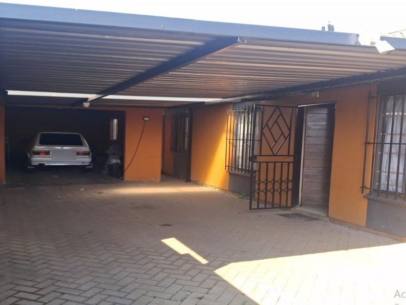 Covered carport area with paved driveway, security gates, and burglar bars on windows.