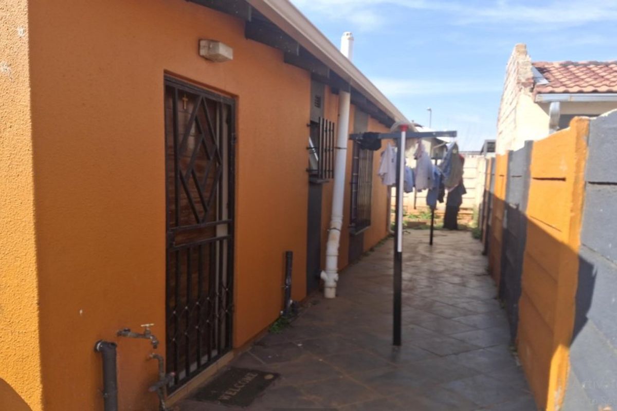 Side exterior area featuring a tiled walkway, security gate, and precast boundary walling.