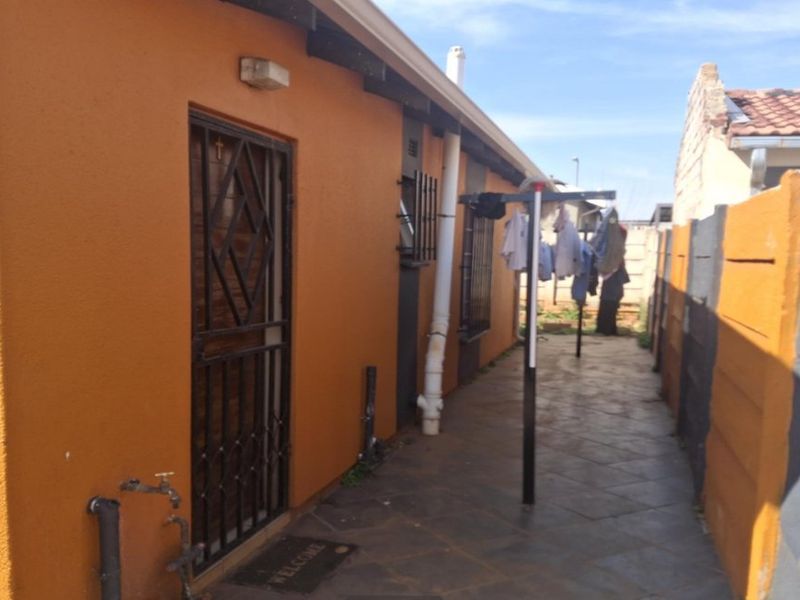 Side exterior area featuring a tiled walkway, security gate, and precast boundary walling.