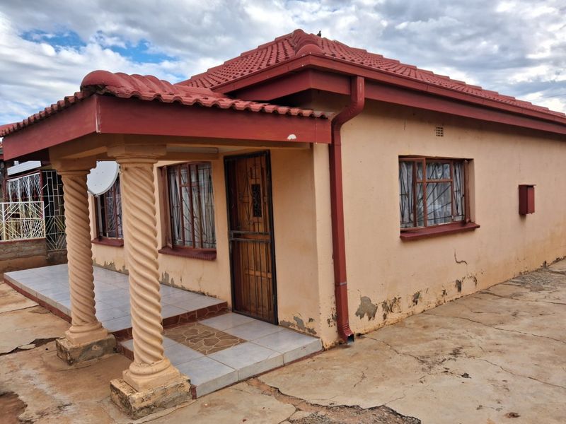 Front view of a single-story house featuring a covered porch with decorative columns, tiled roof, and security features on windows and doors.