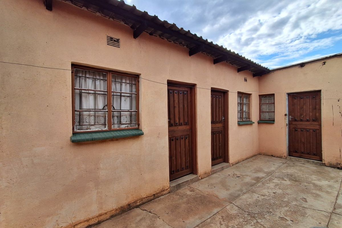 Rear exterior view of the property featuring a paved courtyard, timber doors with security bars, and a corrugated roof structure.