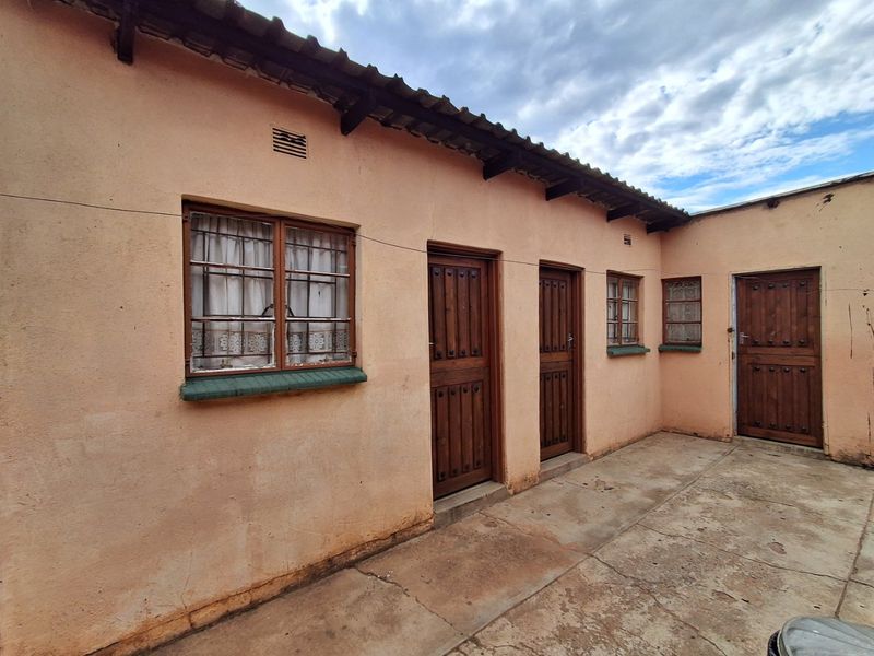 Rear exterior view of the property featuring a paved courtyard, timber doors with security bars, and a corrugated roof structure.