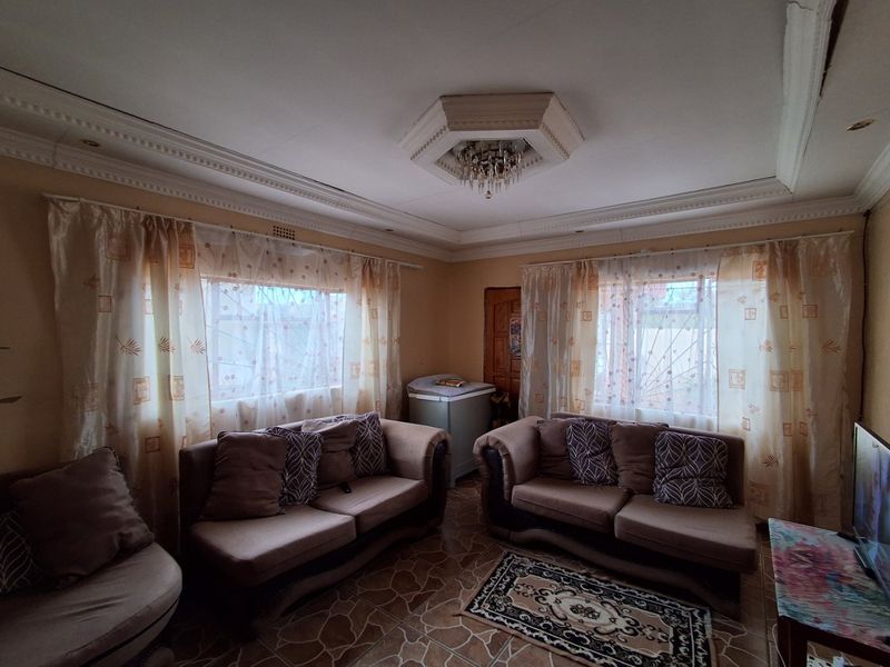 A living room featuring decorative crown molding, a central ceiling rose with chandelier, and tiled flooring, offering a traditional layout with ample natural light.