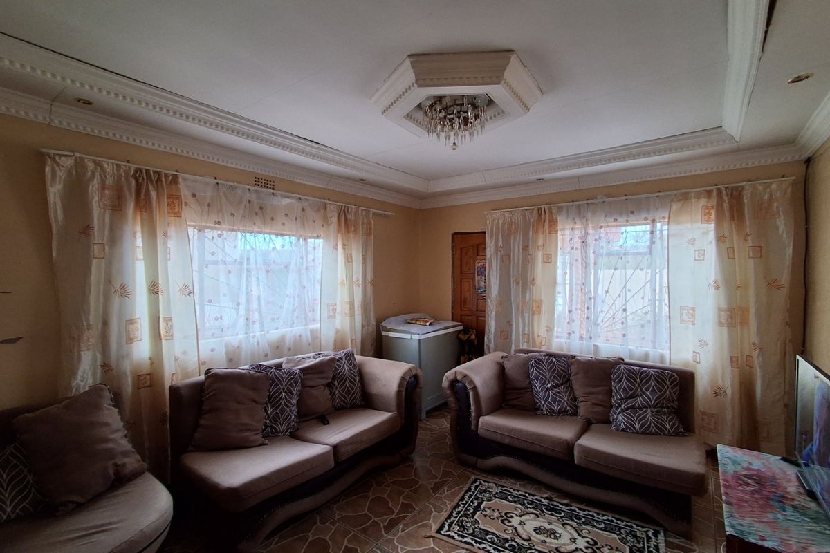 A living room featuring decorative crown molding, an ornate ceiling rose with a chandelier, and tiled flooring.