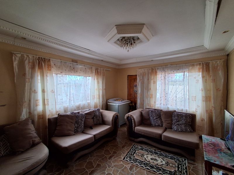 A living room featuring decorative crown molding, an ornate ceiling rose with a chandelier, and tiled flooring.