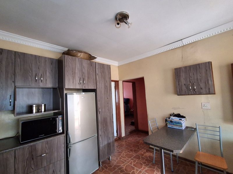 A compact kitchen area featuring wood-look cabinetry, tiled flooring, and ceiling cornicing, currently showing signs of wear and requiring cosmetic updates.