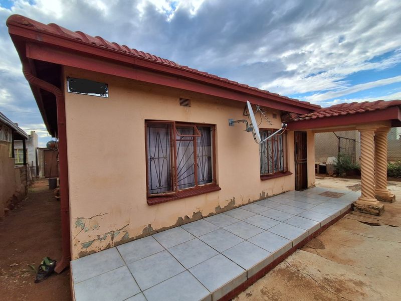 Rear exterior view of the house featuring a tiled patio area, decorative columns, and metal security bars on the windows.