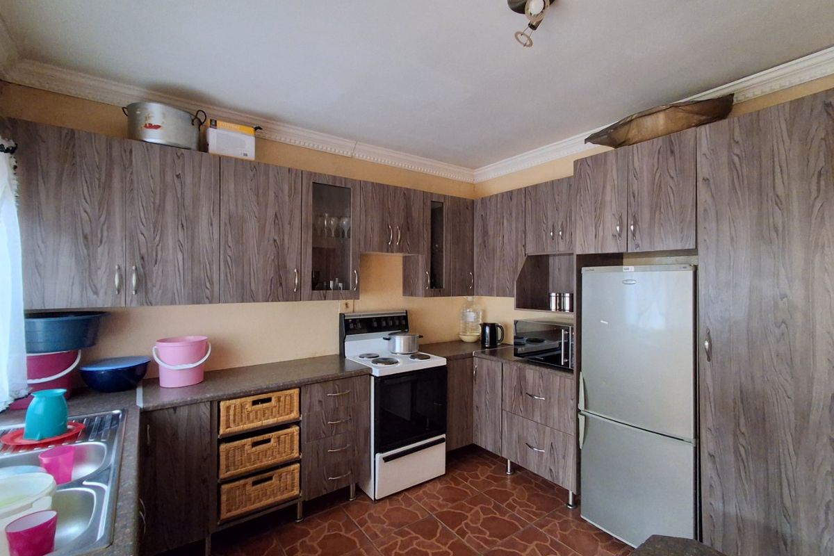 A functional kitchen featuring wood-grain laminate cabinetry, tiled flooring, built-in oven, and a stainless steel sink with ample storage space.