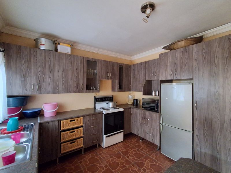 A functional kitchen featuring wood-grain laminate cabinetry, tiled flooring, built-in oven, and a stainless steel sink with ample storage space.