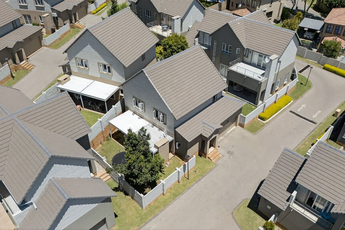 Aerial view of a residential estate featuring multiple detached houses with tiled roofs, paved driveways, and private garden spaces.