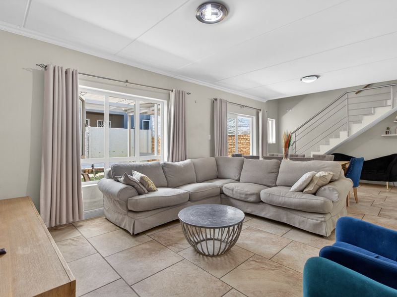 Spacious open-plan living area featuring tiled flooring, a modern staircase with metal balustrades, and large windows providing ample natural light.