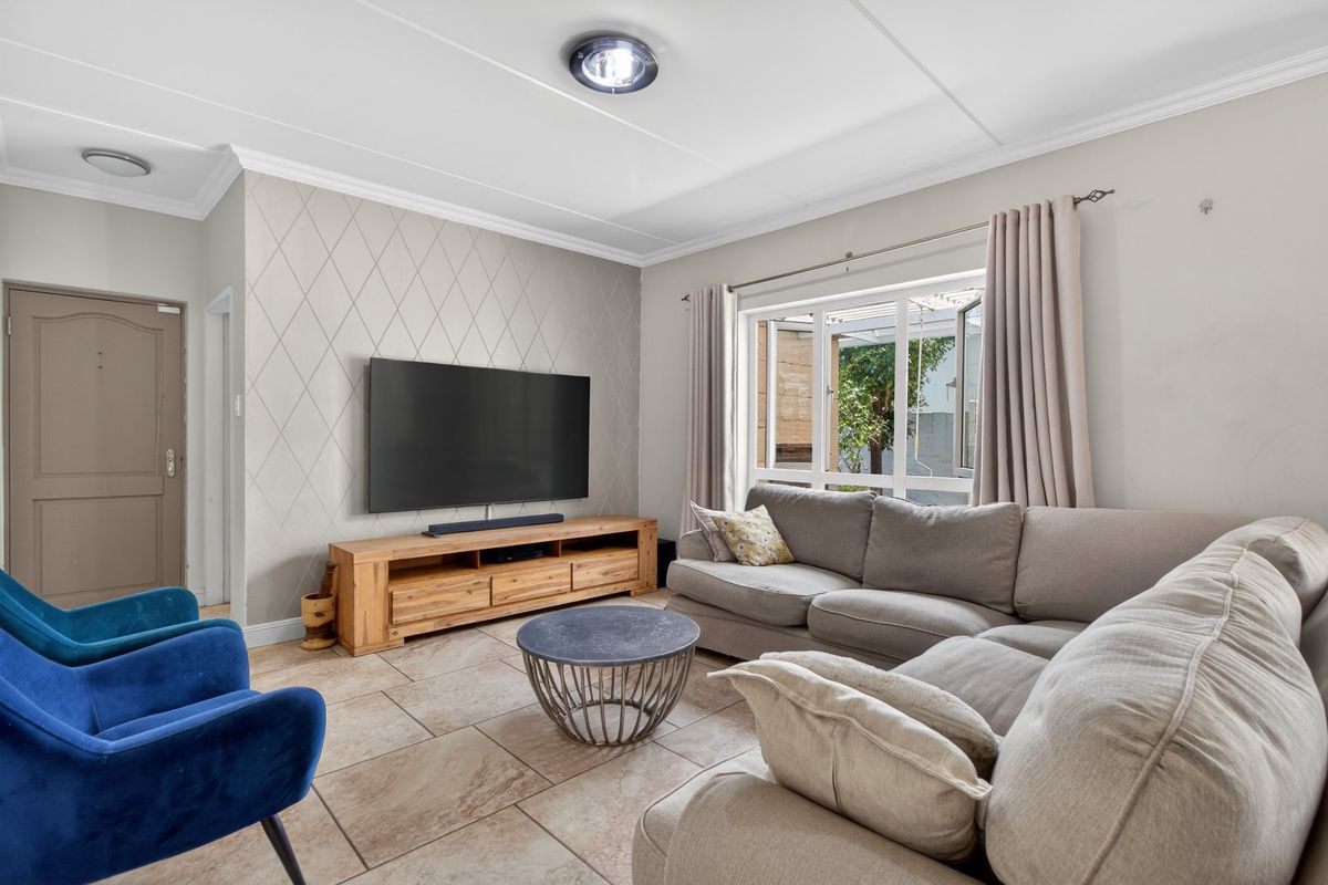 A well-maintained living room featuring tiled flooring, a textured feature wall, and a large window providing natural light and garden views.