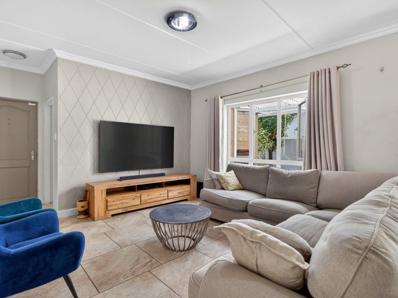 A well-maintained living room featuring tiled flooring, a textured feature wall, and a large window providing natural light and garden views.