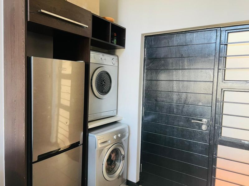 A functional laundry area featuring built-in cabinetry for appliance storage and a secure external door with a metal security gate.