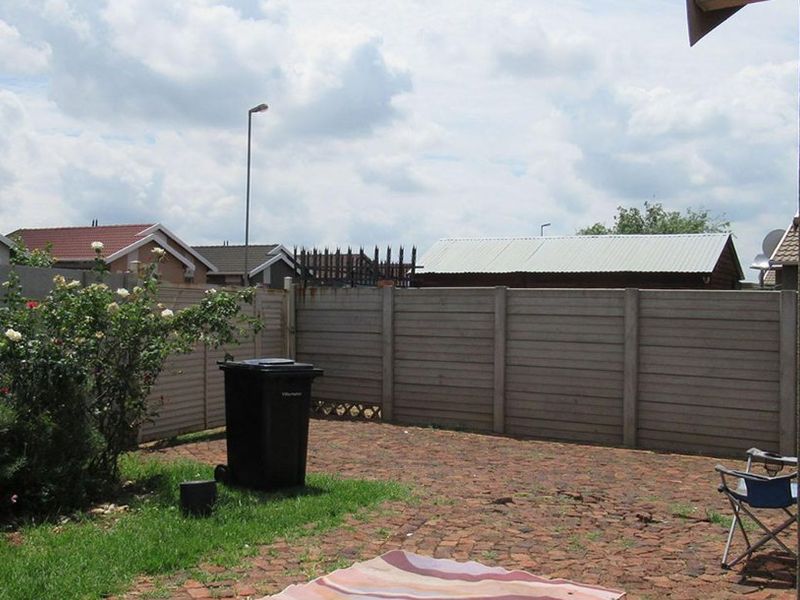 A rear garden area featuring a brick paved patio, lawn, and precast concrete boundary walling.