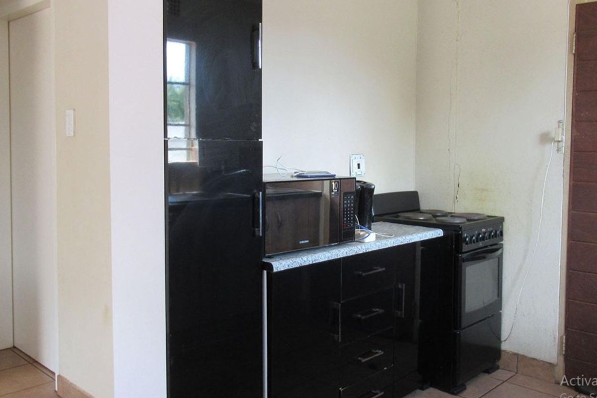 A compact kitchen area featuring black cabinetry, a laminate countertop, and a freestanding electric stove, with visible wall damage requiring maintenance.