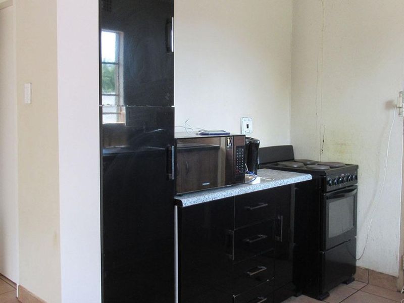 A compact kitchen area featuring black cabinetry, a laminate countertop, and a freestanding electric stove, with visible wall damage requiring maintenance.