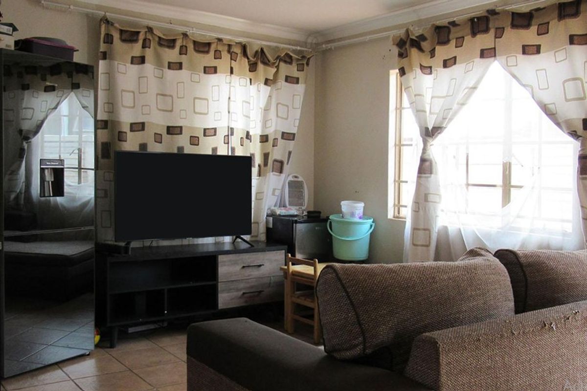 A functional living room featuring tiled flooring and windows fitted with security burglar bars, providing a practical and secure living space.