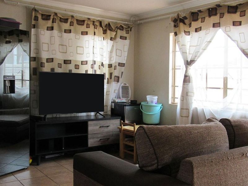 A functional living room featuring tiled flooring and windows fitted with security burglar bars, providing a practical and secure living space.