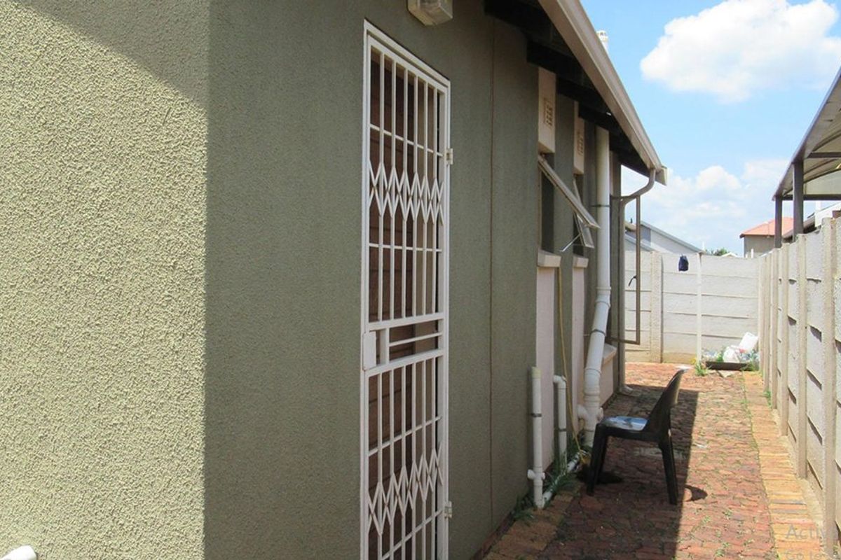 Side exterior view of the property featuring a security gate, brick paving, and precast concrete boundary walling.