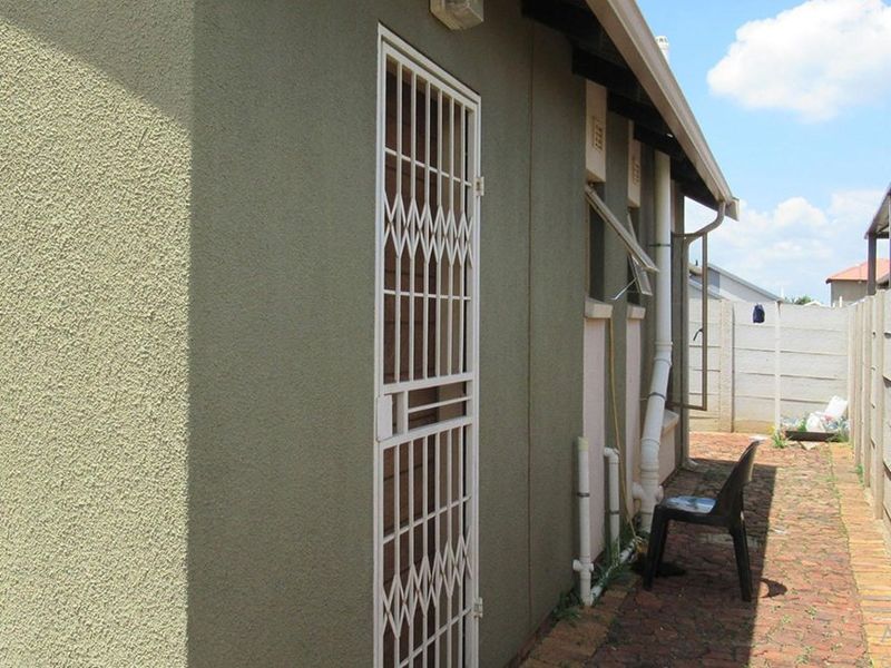 Side exterior view of the property featuring a security gate, brick paving, and precast concrete boundary walling.