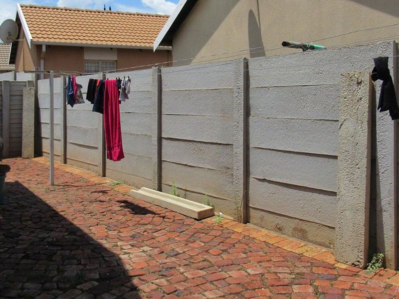 A narrow rear exterior area featuring brick paving and a precast concrete boundary wall with a fixed washing line.