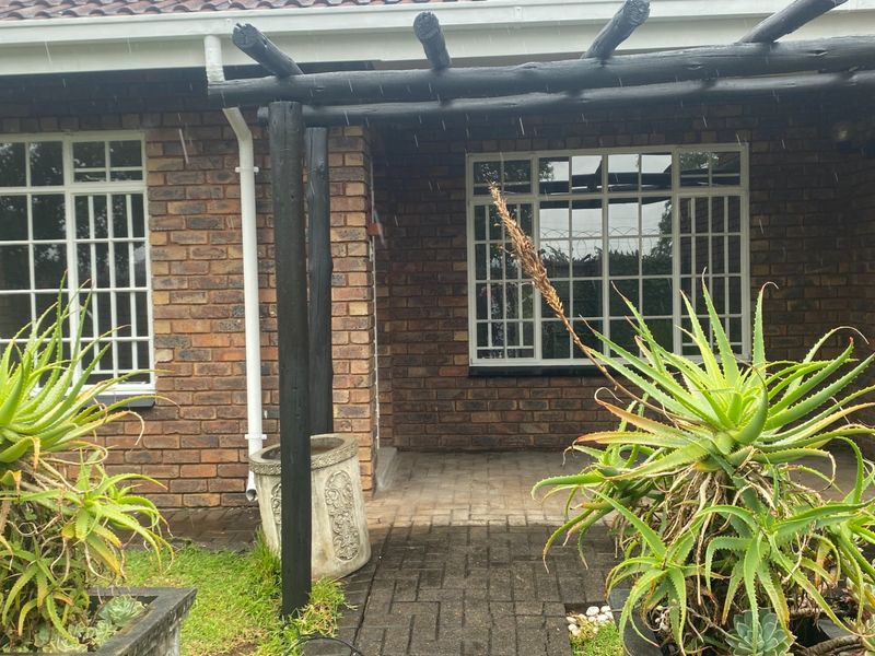 Front entrance area featuring a brick facade, a timber pergola, and a paved walkway leading to the main entry.