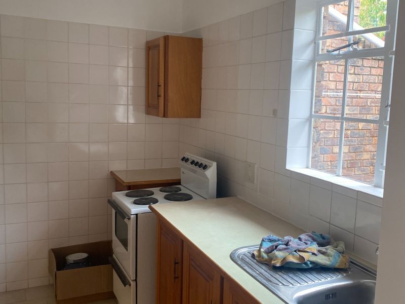 A functional kitchen featuring tiled splashbacks, wooden cabinetry, laminate countertops, and a freestanding stove, offering potential for modern renovation.