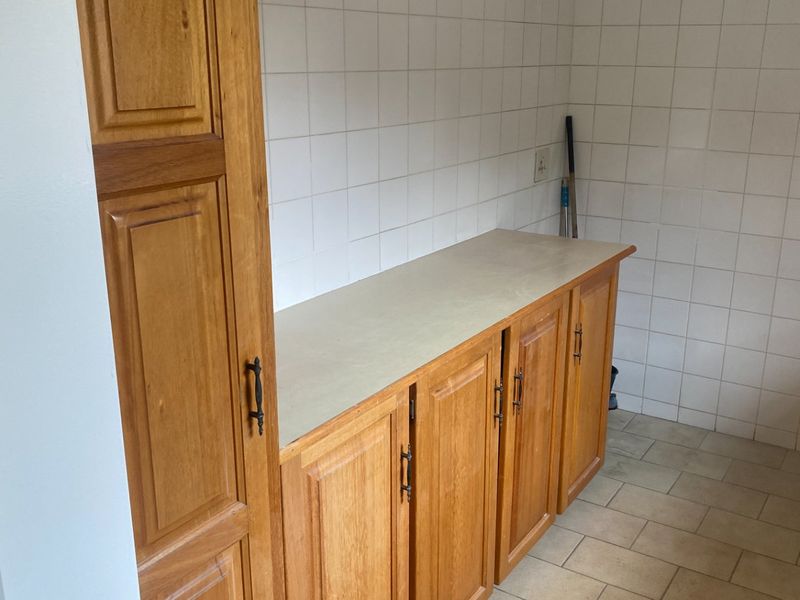 A functional scullery or utility area featuring traditional wooden cabinetry, laminate countertops, and tiled wall and floor finishes.