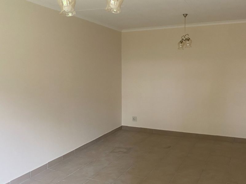 A spacious, empty living area featuring neutral walls, tiled flooring, and existing ceiling light fixtures, ready for personalization.