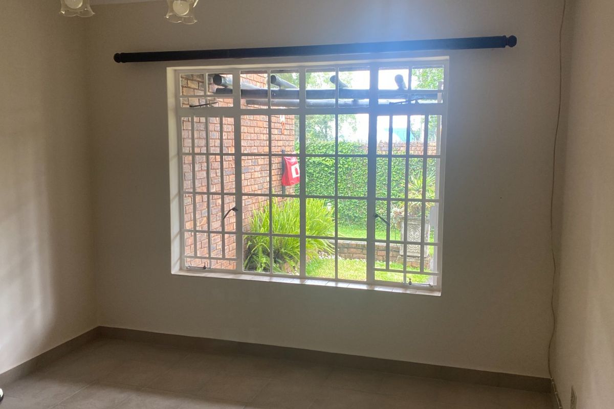 A bright, empty living room featuring large windows with security bars, tiled flooring, and a view of the private garden area.