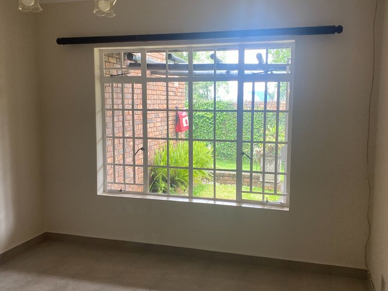 A bright, empty living room featuring large windows with security bars, tiled flooring, and a view of the private garden area.