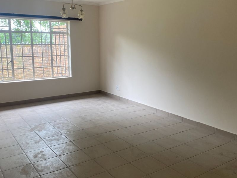 A spacious, empty living room featuring neutral tiled flooring, large windows with security bars, and clean wall finishes, ready for personalization.