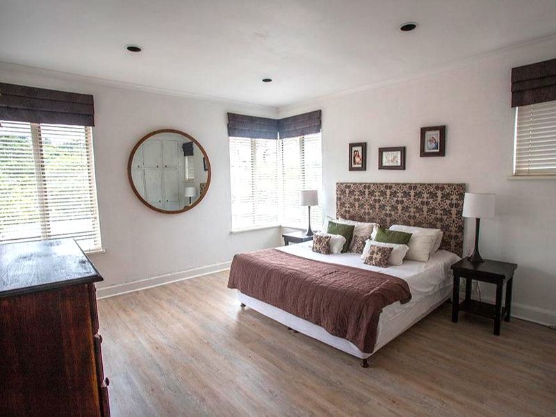 A well-lit bedroom featuring laminate flooring, recessed downlights, and venetian blinds, offering a clean and comfortable living space.