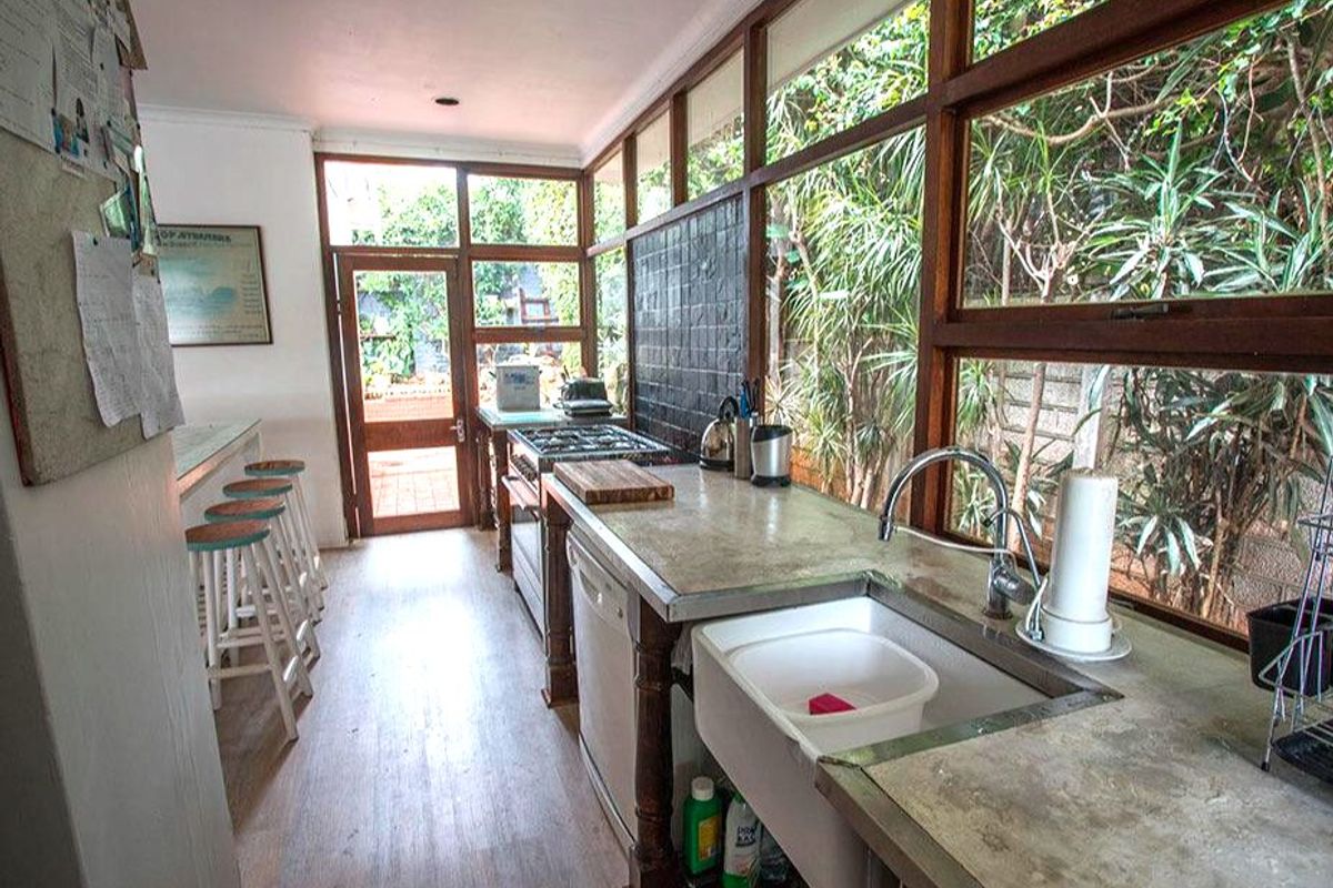 A galley-style kitchen featuring a farmhouse sink, gas hob, and extensive timber-framed windows overlooking the garden, offering a bright and functional workspace.