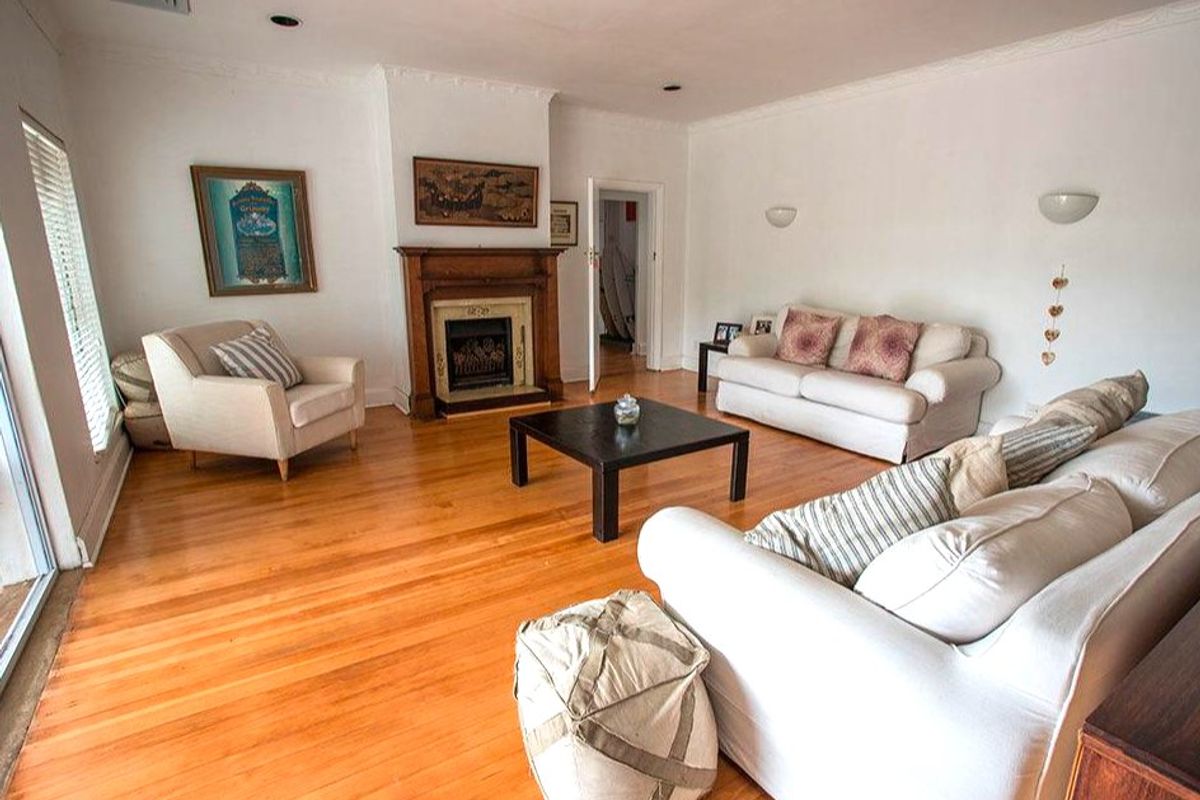 Spacious living room featuring polished hardwood flooring, a classic fireplace with a timber mantelpiece, and elegant crown molding details.