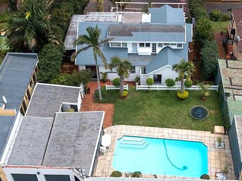 Aerial view of a residential property featuring a swimming pool, landscaped garden, detached garage, and a multi-level house with a pitched roof.
