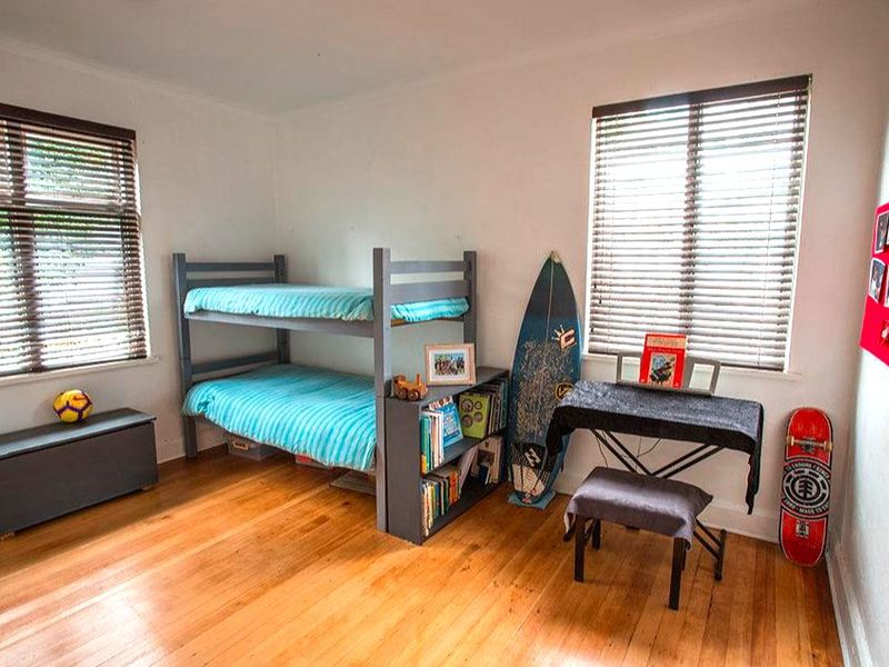 A bedroom featuring polished timber flooring and dual windows with venetian blinds, offering a bright and functional living space.