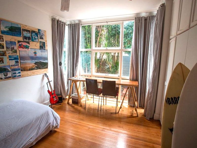 A bedroom featuring polished timber flooring, built-in storage cupboards, and a large window providing natural light and garden views.