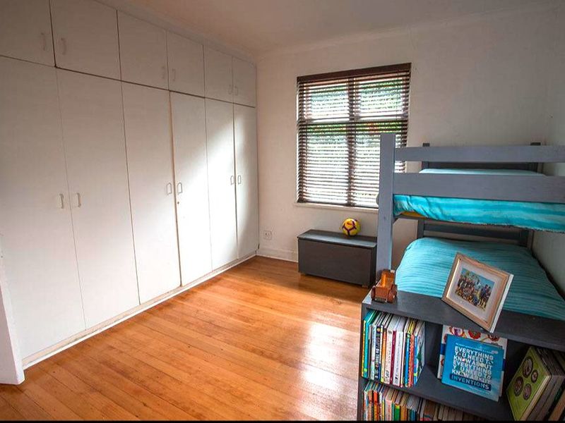 A bedroom featuring timber flooring, built-in cupboards providing ample storage, and a window fitted with venetian blinds.