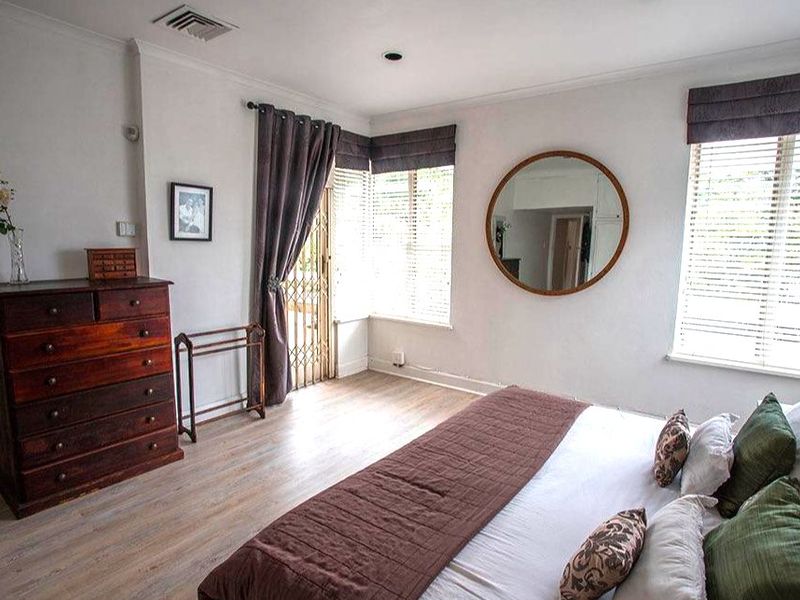 A well-lit bedroom featuring laminate flooring, venetian blinds, and a security gate leading to an outdoor area.