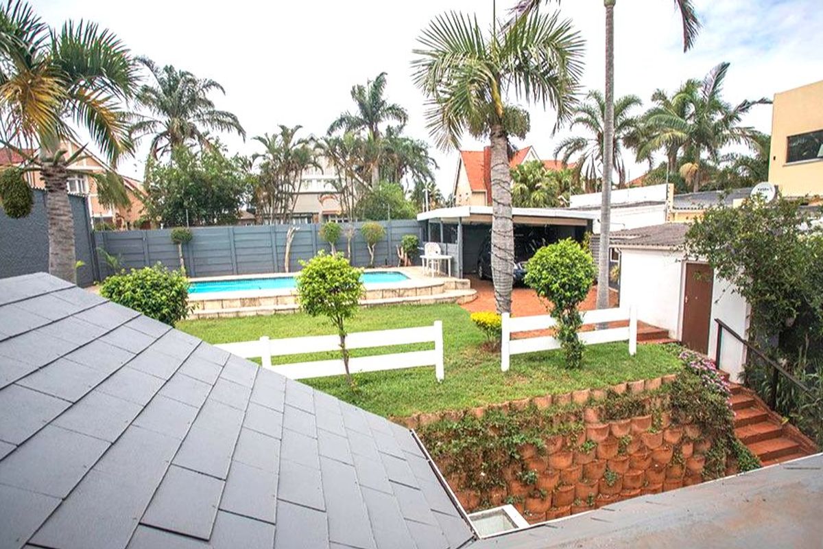 Rear exterior view featuring a swimming pool, lawn area, retaining wall, and a covered carport structure.