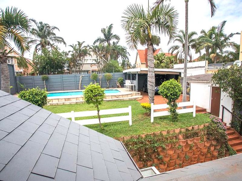 Rear exterior view featuring a swimming pool, lawn area, retaining wall, and a covered carport structure.