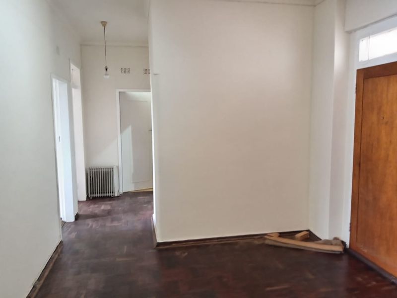 An empty hallway featuring dark parquet flooring, a wooden entrance door, and a wall-mounted radiator.
