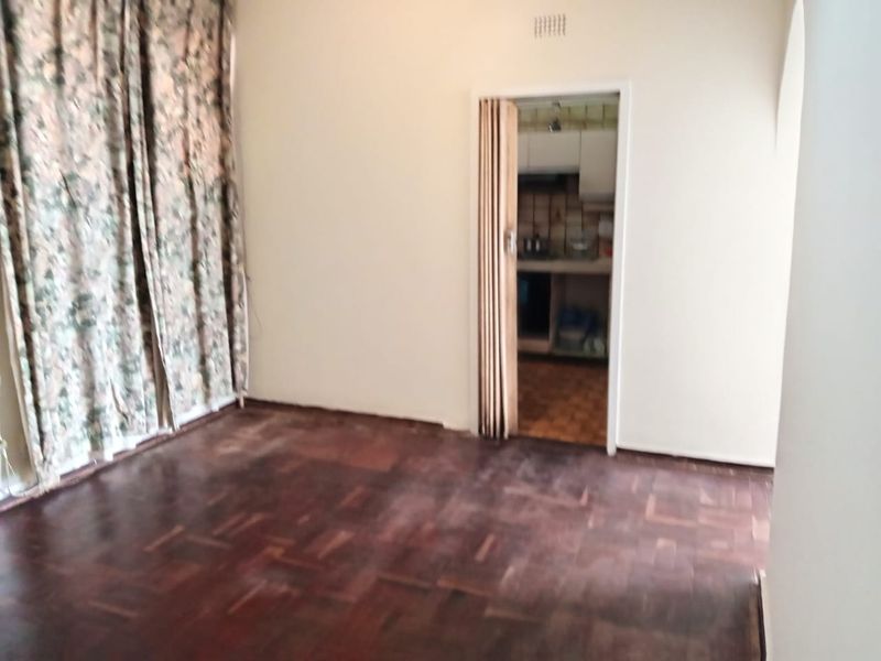 An empty living room featuring original parquet flooring and a folding door leading to the kitchen area.
