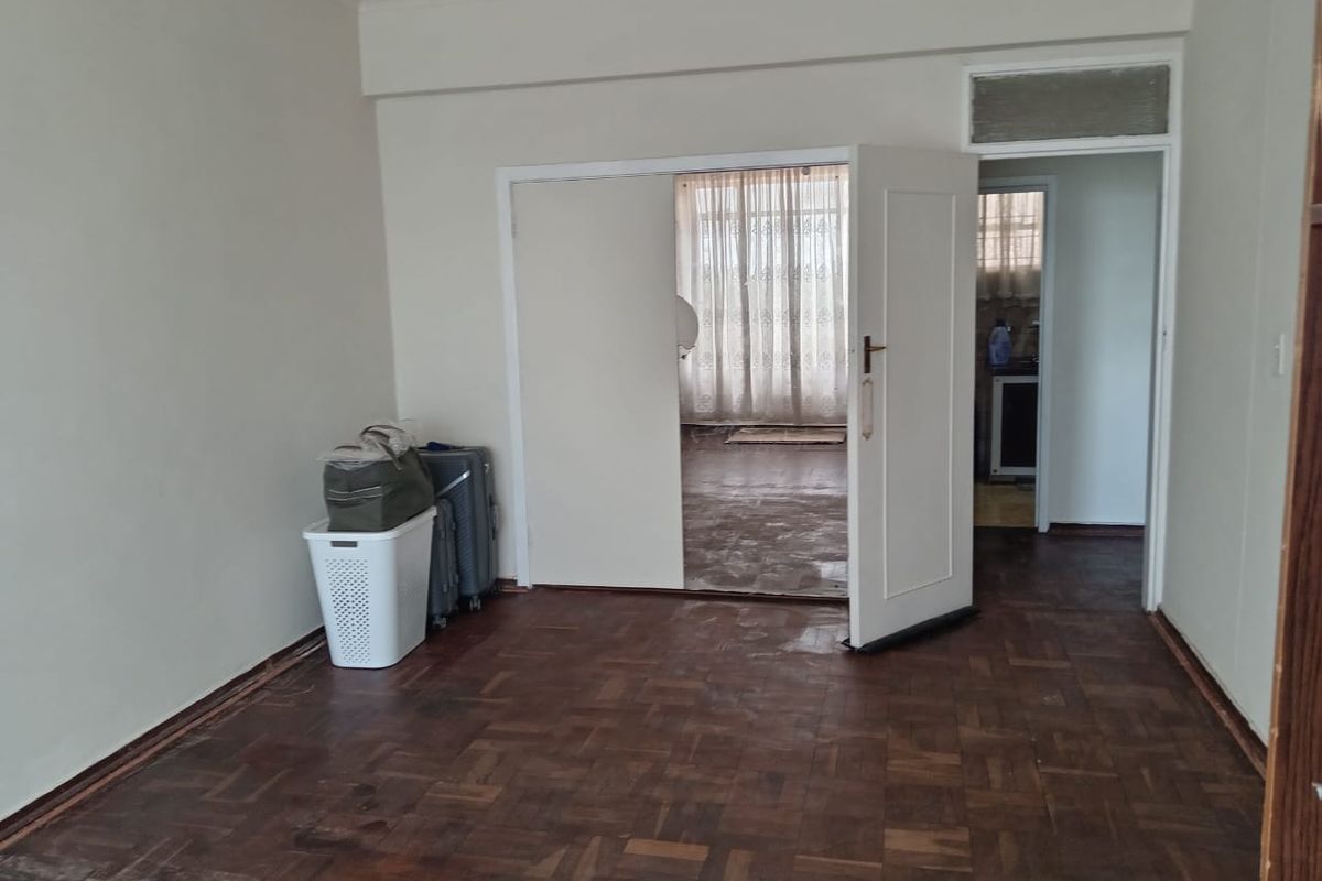 An empty living room featuring original parquet flooring and an internal door leading to an adjacent space.