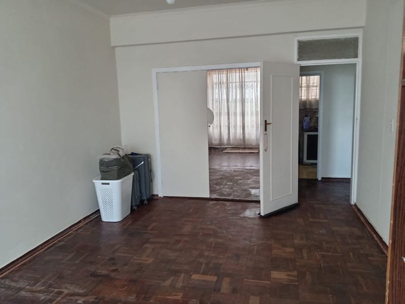 An empty living room featuring original parquet flooring and an internal door leading to an adjacent space.