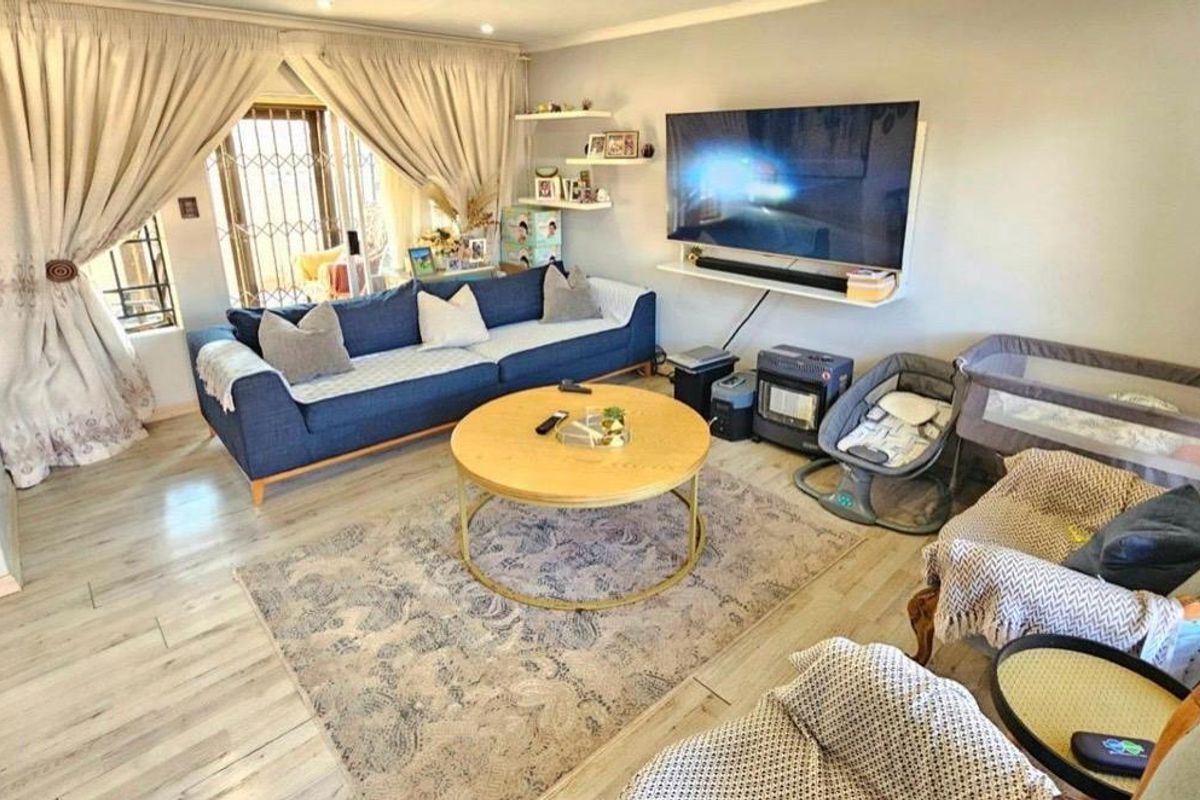 A comfortable living room featuring light-toned laminate flooring, recessed ceiling lighting, and a secure window with a fitted security gate.