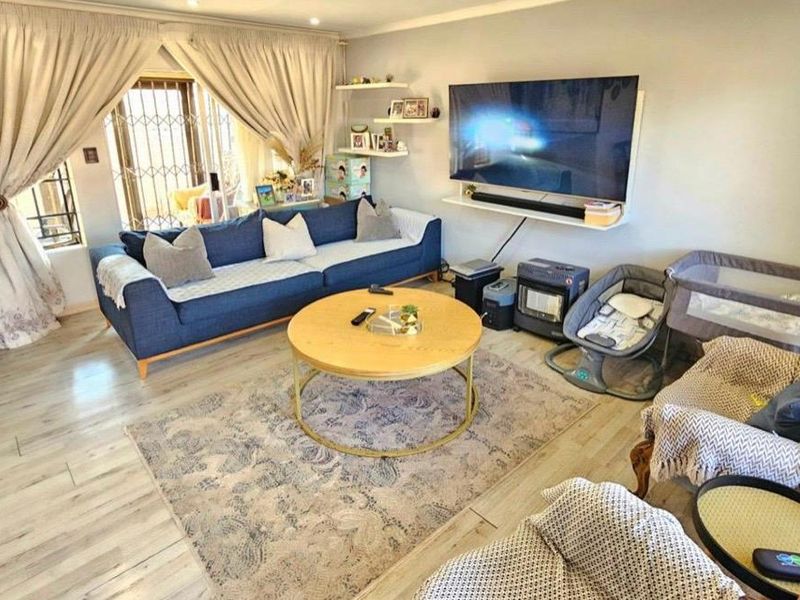 A comfortable living room featuring light-toned laminate flooring, recessed ceiling lighting, and a secure window with a fitted security gate.